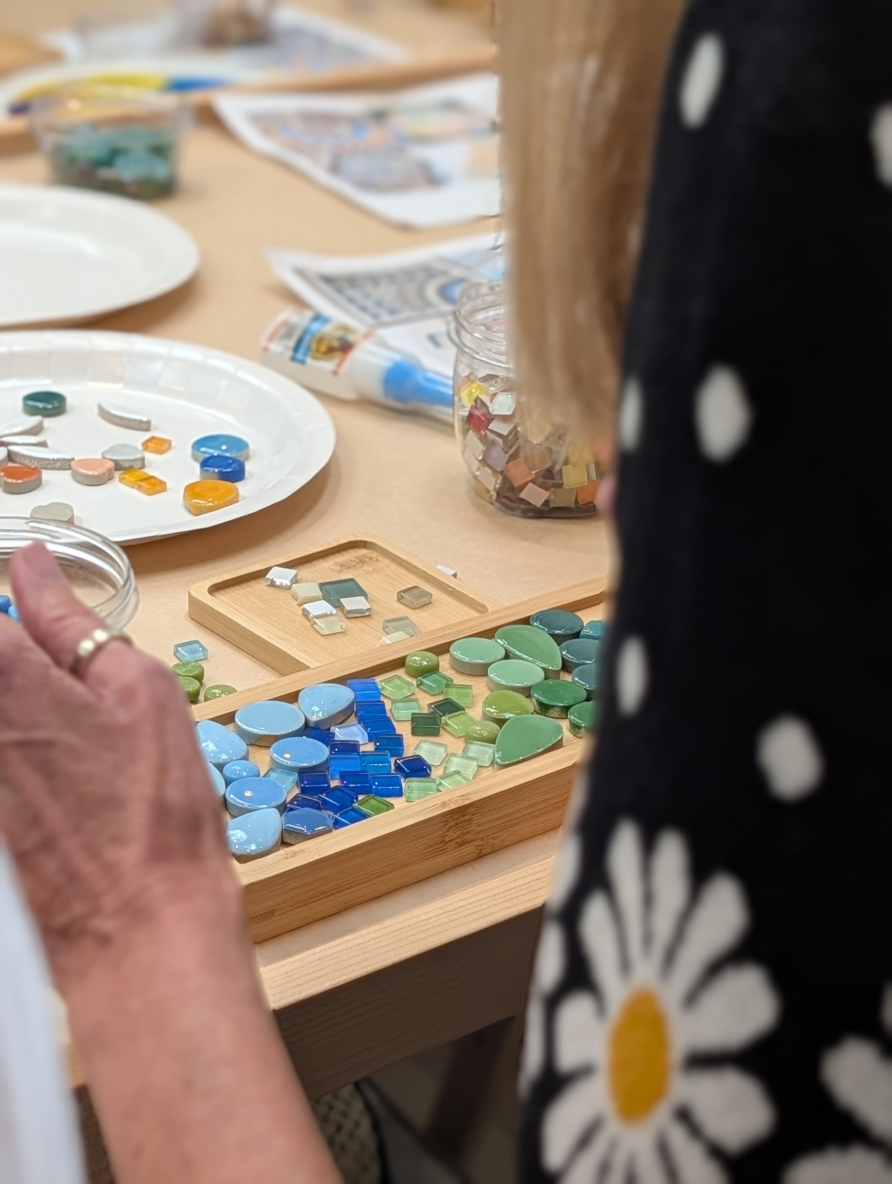 Person working on a mosaic art project with colorful tiles on a wooden board.
