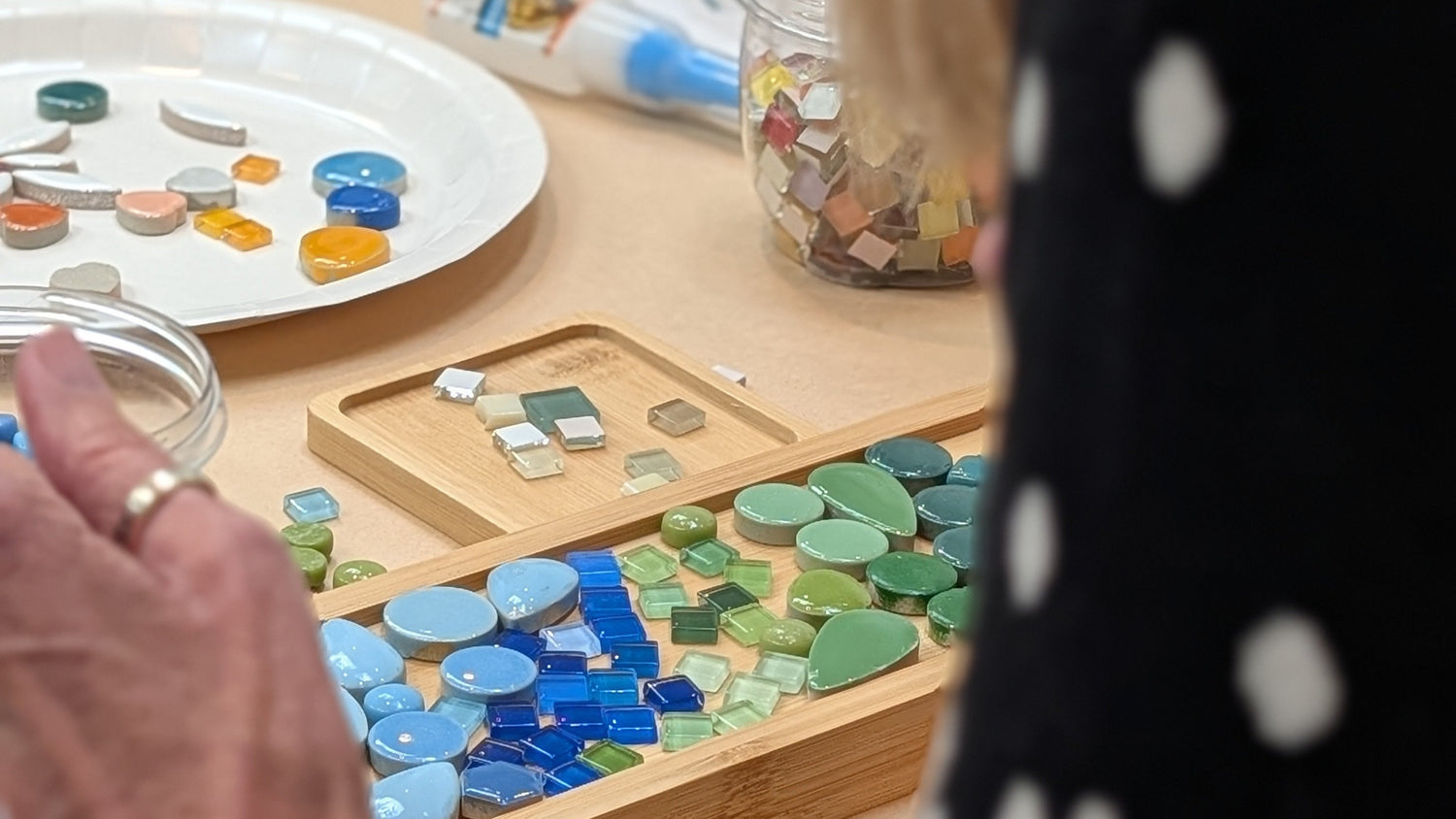 Person working on a mosaic art project with colorful tiles on a wooden board. Wendy Cardiff Creative Workshops in Victoria, BC.